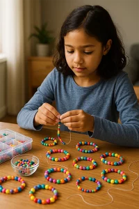 A young girl sits at a wooden table at home, threading colourful beads onto a string to make bracelets, with finished bracelets and bowls of beads spread out around her.